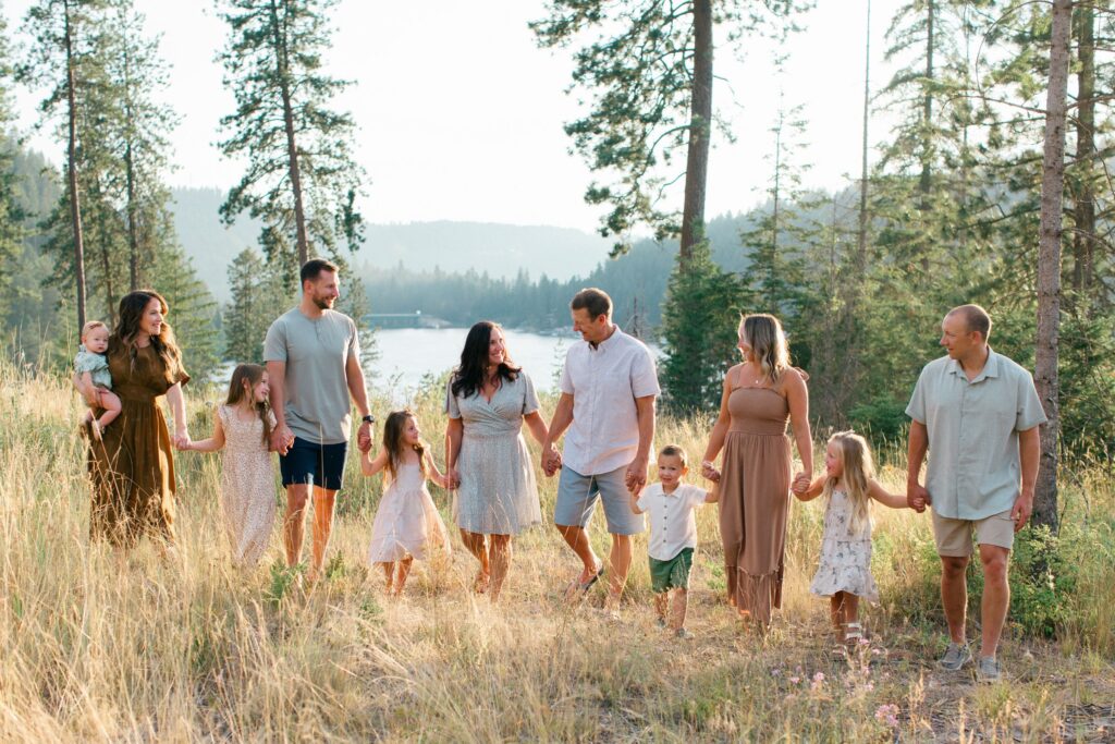 extended family holding hands and walking across a field in the mountains at sunset in coeur dalene