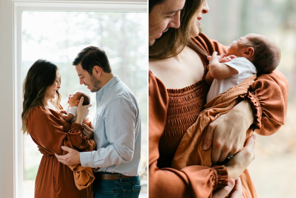 mom and dad in their living room with natural light pouring in, holding and smiling at their newborn baby for indoor newborn photography session in CDA
