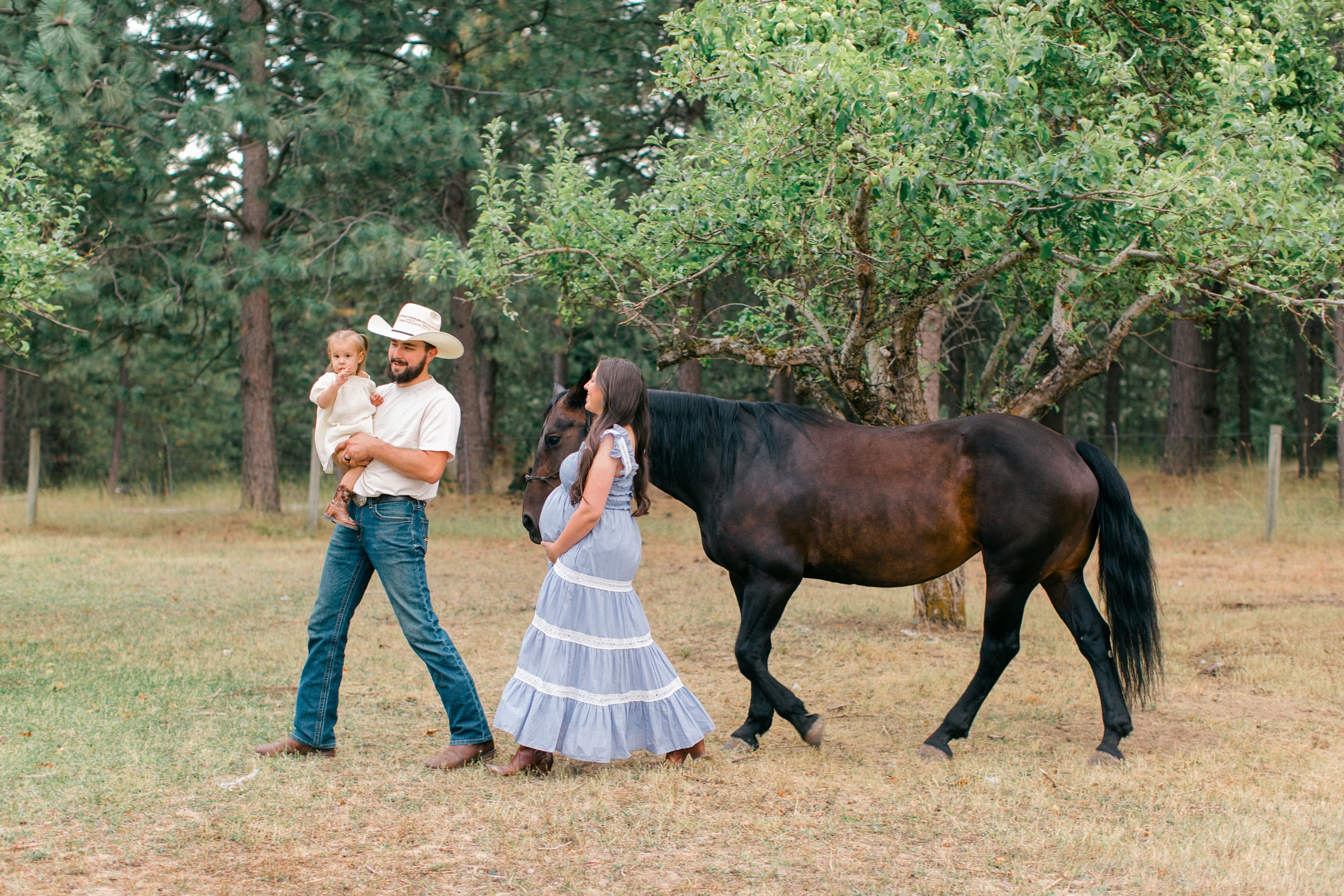 Pregnant woman and family walking with a horse in a peaceful farm setting during a Coeur d'Alene maternity photography session