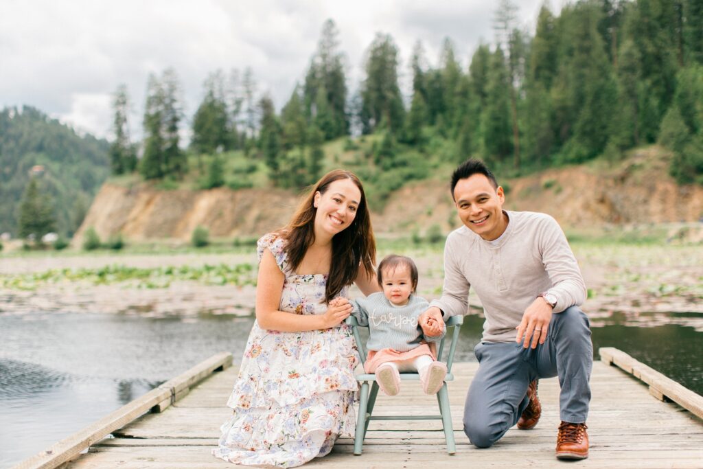 mom and dad with one year old crouching and smiling at the camera during a family vacation to lake coeur d'alene idaho