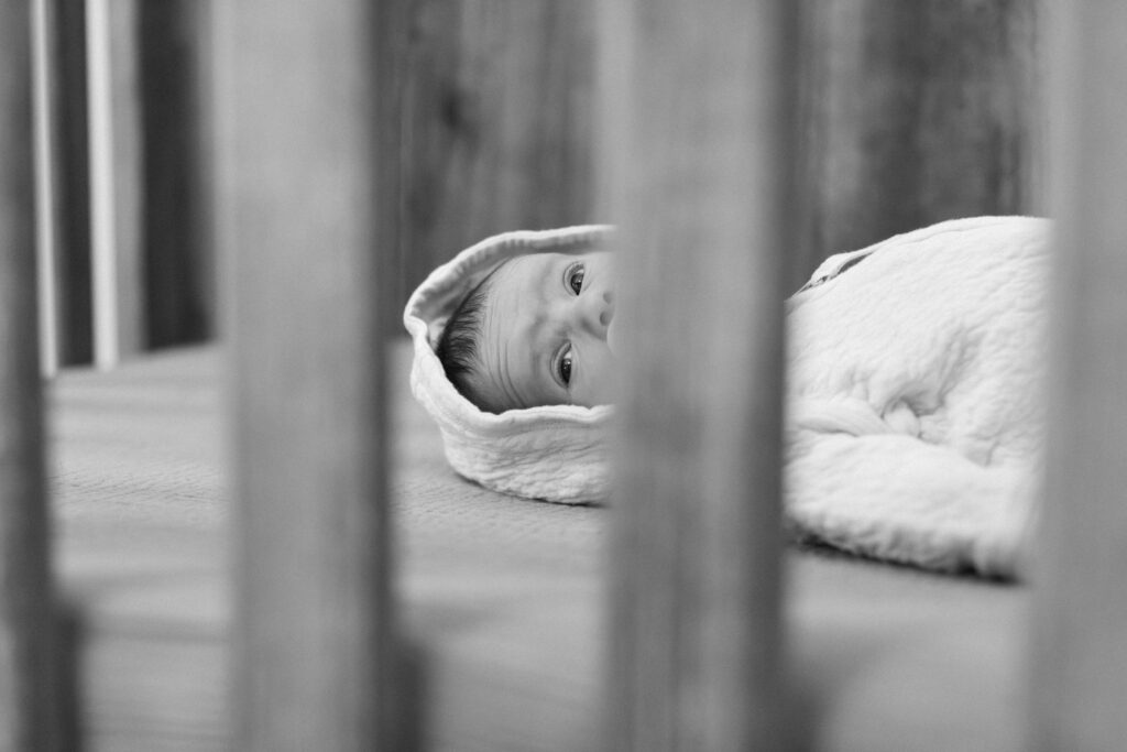 newborn peeking through her crib in her nursery